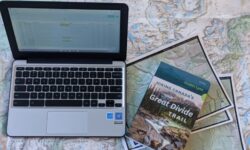 A laptop surrounded by maps and a GDT guidebook